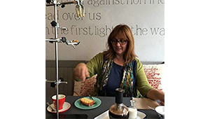 Deb Alma sitting at a table with refreshment and a manuscript