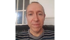 David Longworth sitting in front of a square window and looking into the camera