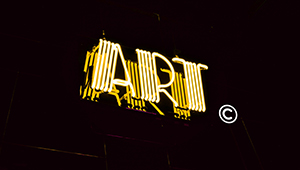 A yellow neon sign over a dark backdrop which reads ART and has a copyright symbol