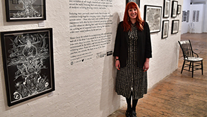 Jennifer Gilbert standing in front of a large inscription on a wall in an art gallery