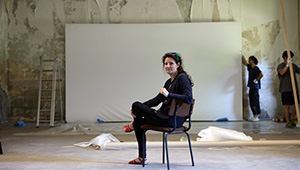Dr Kate McMillan sitting in a chair in front of a large, blank canvas