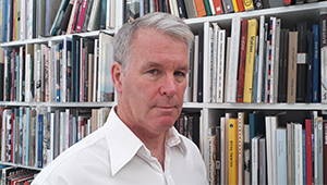 Stephen Snoddy facing the camera in front of rows of bookshelves