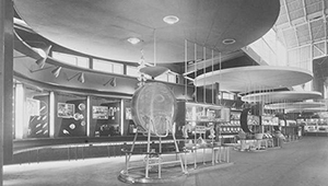 A white room full of glass chairs, tables, plates, lights and windows