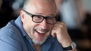 Tony Heaton, wearing glasses, a watch and a blue button-up shirt