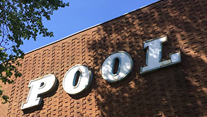 A brick building with a sign reading POOL in white block capitals on its side