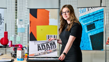 A photograph of a female art student with long brown hair and wearing glasses she is looking through a collection of artwork within a folder